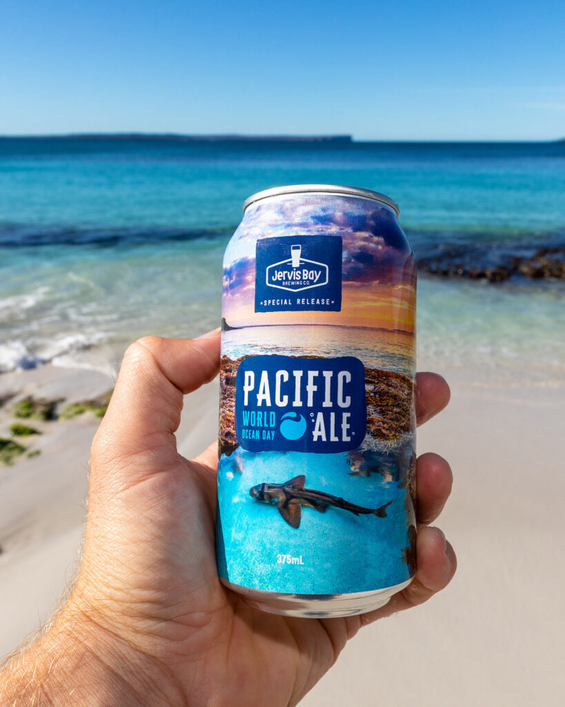 Can of World Ocean Day Pacific Ale being held in a hand with Jervis Bay and Point Perpendicular in the background